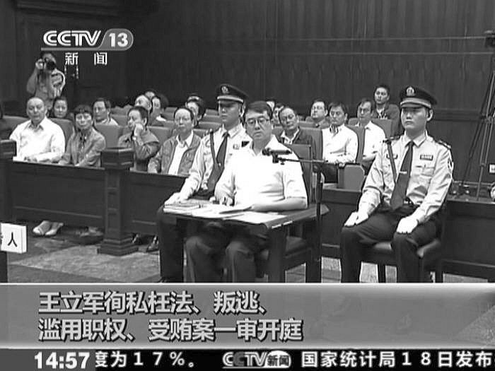 In a screen grab from a video released by Chinese Central TV, Wang Lijun is seen at his trial on Sept. 18, in Chengdu, China. The Chinese characters at the bottom of the image list the four charges against Wang. (Epoch Times)