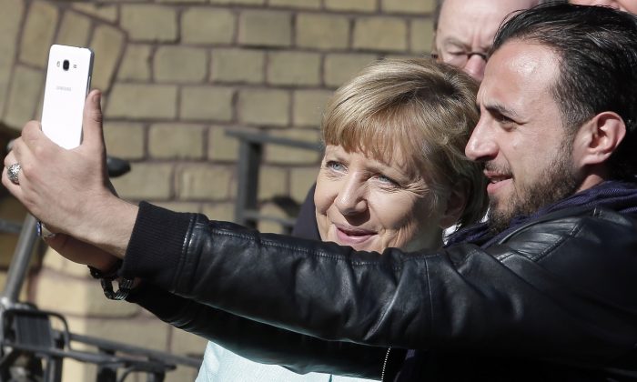 An unidentified man takes a picture of himself and German Chancellor Angela Merkel, left, during Merkel's visit at a registration center for migrants and refugees in Berlin, Germany, Thursday, Sept. 10, 2015. (AP Photo/Michael Sohn)