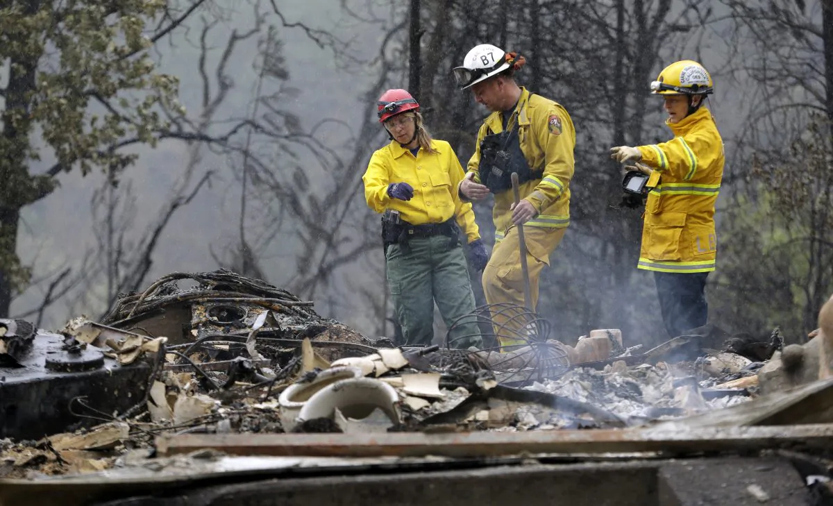 Firefighter Sean Norman, center, and search dog handlers Mary Cablk, left, and Lynne Engelbert look over the remains of a home in the Anderson Springs area, Wed., Sept. 16, 2015, near Middletown, Calif. (AP Photo/Elaine Thompson)