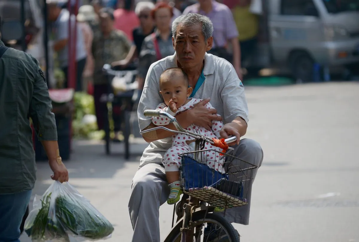 An elderly man holds a baby in his arms as he rides a bicycle along a road in Beijing on September 8, 2015. (WANG ZHAO/AFP/Getty Images)