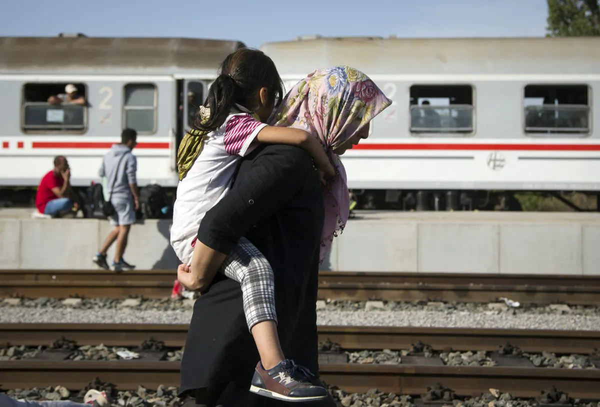 A refugee woman carries a child at a train station in Beli Manastir, near Hungarian border, northeast Croatia, early Friday, Sept. 18, 2015. Croatian police say some 13,300 migrants have entered the country from Serbia since the first groups started arriving more than two days ago. (AP Photo/Darko Bandic)