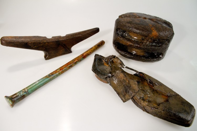Artifacts recovered from HMS Investigator, from left to right: a wooden horn cleat, which the ropes would have been looped around for tying the vessel's rigging, a copper alloy bolt used to fasten ship timbers, a leather shoe, and a double-sheave pulley (Louis Barnes/Parks Canada ) Artifacts recovered from HMS Investigator, from left to right: a wooden horn cleat, which the ropes would have been looped around for tying the vessel's rigging, a copper alloy bolt used to fasten ship timbers, a leather shoe, and a double-sheave pulley (Louis Barnes/Parks Canada )