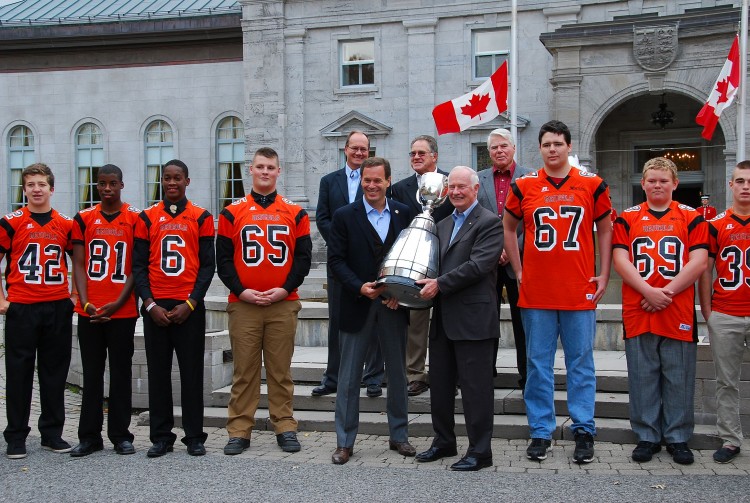 Canadian Football League (CFL) Commissioner Mark Cohon (L) and Governor General of Canada David Johnston hold the Grey Cup outside Rideau Hall, the Governor General's official residence, alongside members of the Orleans Bengals Football Club and former CFL greats, on Oct. 21, 2012. (Jonathan Ren/The Epoch Times)