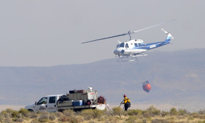 FILE - In this Aug. 14, 2015 file photo, a helicopter flies past a ground crew fighting a wildfire scorching grassland that ranchers need to feed cattle and which is also primary habitat for sage grouse, near the Reynolds Creek area in the Owyhee Mountains of Idaho. (Adam Eschbach/The Idaho Press-Tribune via AP, File) 