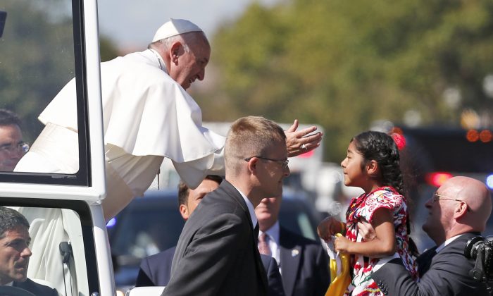 Pope Francis reaches from the popemobile for a child that is brought to him, during a parade in Washington, Wednesday, Sept. 23, 2015. (AP Photo/Alex Brandon, Pool)