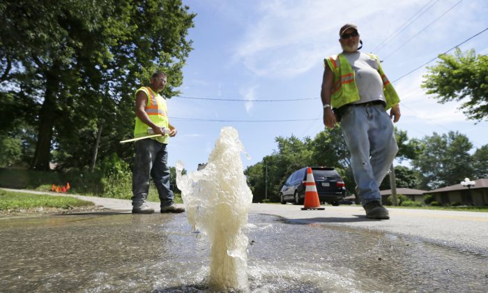 Des Moines Water Works employees walk past water bubbling through a hole in a street following a water main break in Des Moines, Iowa on Wed., July 29. (AP Photo/Charlie Neibergall)