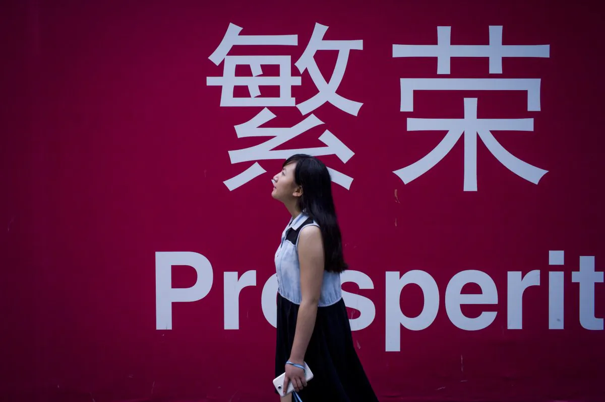 A woman walks beside a board with the characters for "prosperity" in Chinese in Beijing on July 28, 2015. (FRED DUFOUR/AFP/Getty Images)