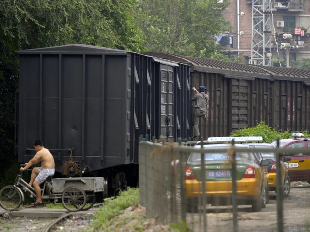 A man rides a tricycle over the rails next to a cargo train in Beijing 