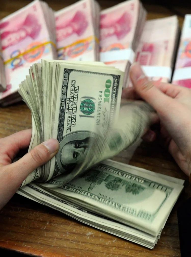 A Chinese bank worker counts a stack of U.S. dollars together with stacks of 100 Chinese yuan notes. China is driving up its national debt to finance its foreign currency reserves, the largest in the world. (STR/AFP/Getty Images)