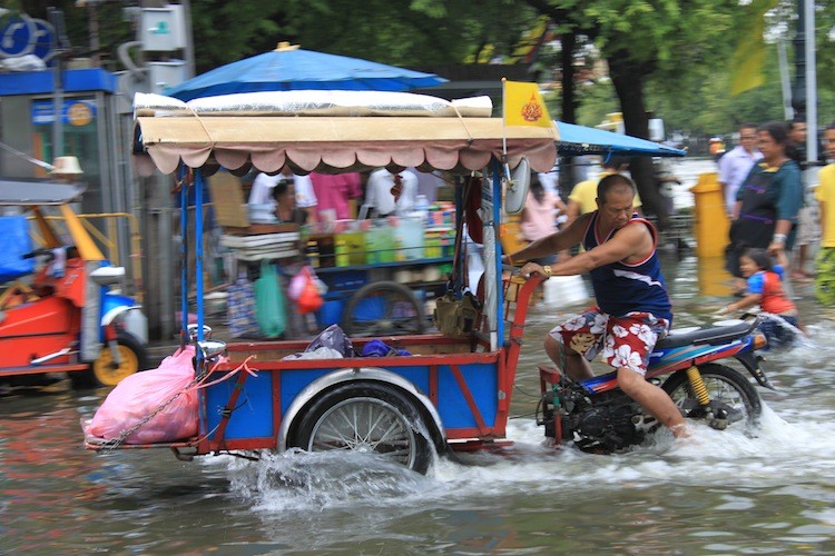 A man looks down as he drives through floodwater covering a street in Bangkok, October.  (Cameron McKinley/The Epoch Times)