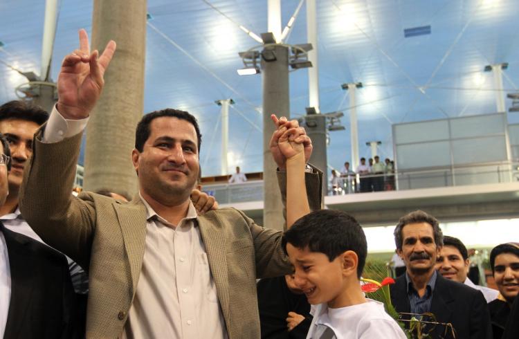 Iranian nuclear scientist Shahram Amiri holds his son's hand as he flashes the victory sign upon arrival at Imam Khomeini Airport in Tehran on July 15.  (Atta Kenare/Getty Images )