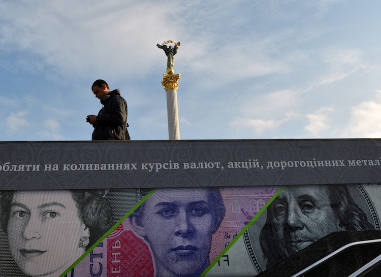 A man stands next to an advertising placard showing British pounds, US dollars and Ukrainian hryvnia banknotes on a warm autumn day in the Kiev, Ukraine, on Nov. 12, 2012. (Sergei Supinsky/AFP/Getty Images) 