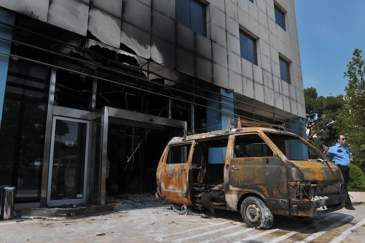 A security officer standA security officer stands by the mini-van used by attackers at entrance to the Microsoft office in an Athens northern suburb on June 27. Attackers targeted the Microsoft main office in the Greek capital in a pre-dawn arson attack Wednesday, smashing the entrance with a mini-van and setting off gas canisters. (Louisa Gouliamkai I/AFP/GettyImages)s by the mini-va Epoch Times Photo