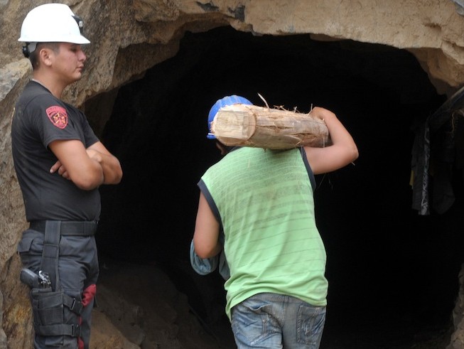 Rescuer carries support post into mine shaft. A policeman stands guard as a rescuer carries a timber post into the mine for use as a tunnel support during an operation to rescue nine miners at the Cabeza de Negro copper mine. (Cris Bouroncle/AFP/Getty Images)