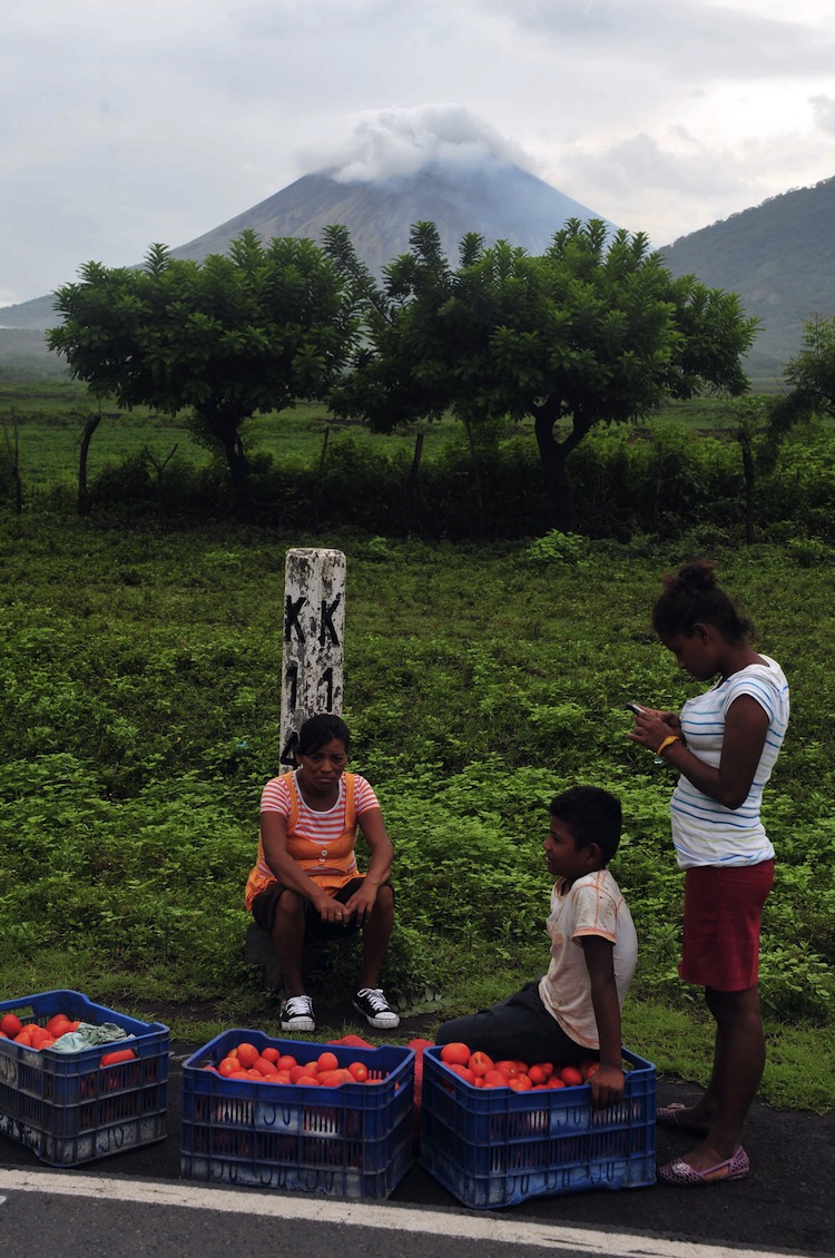 Backdropped by the San Cristobal volcano, people wait for transportation along the Pan American Highway in Chinandega, Chonco sector, Nicaragua, on Sept. 9. On Saturday it rumbled to life with three explosions prompting a column of smoke and ash to rise from its cone and forcing the evacuation of 3,000 residents living on or around its slopes. (Hector Retamal/AFP/GettyImages) Epoch Times Photo