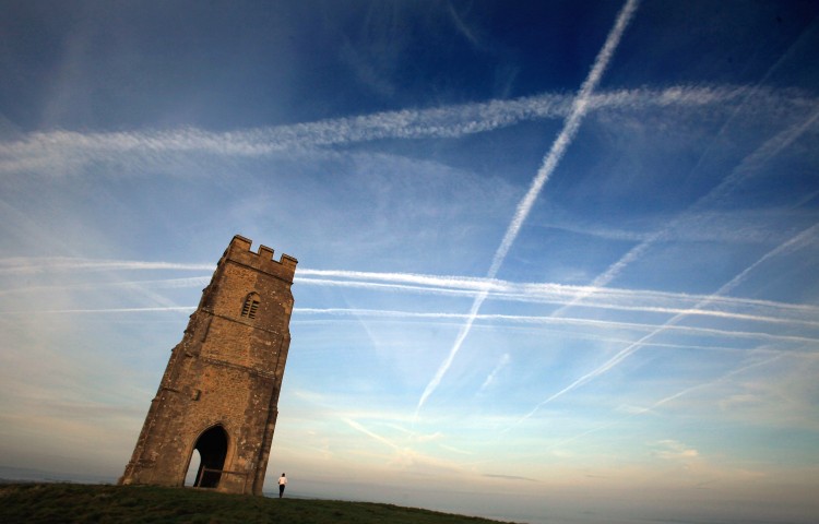 A woman looks up at the mass of contrails left by a jet aircraft crossing the sky above St. Michael's Tower near Glastonbury, England. (Photo by Matt Cardy/Getty Images)
