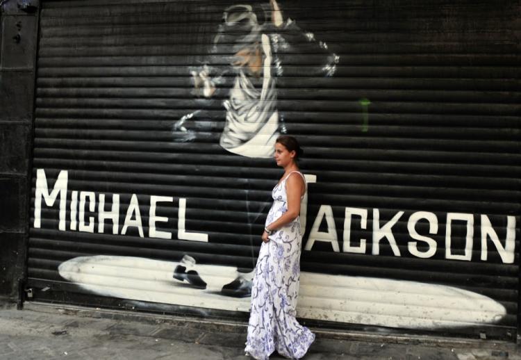 MICHAEL JACKSON BIRTHDAY: A woman poses in front of a graffiti depicting Michael Jackson at shop's shield at Athens flea market area in Monastiraki in Athens. (Louisa Gouliamaki/AFP/Getty Images)