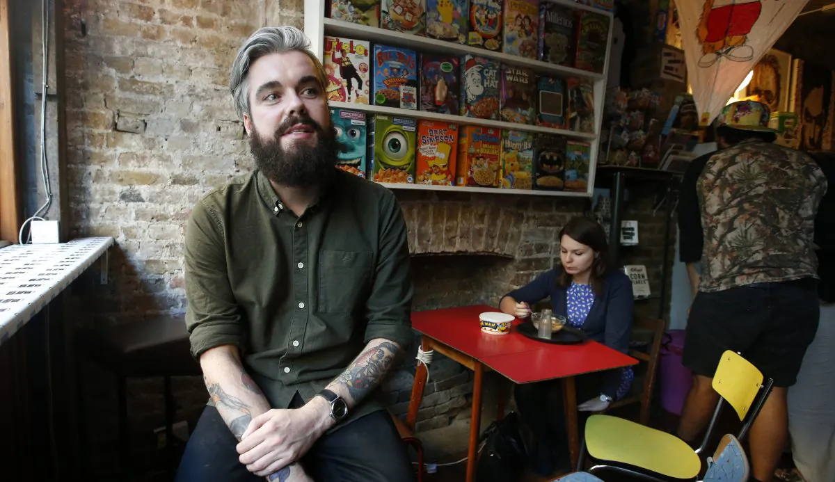 Alan Keery one of the twin brothers who developed and own the Cereal Killer Cafe in  Brick Lane, London talks to the Associated Press at the cafe, as customer Melanie Wolstenholme eats a late afternoon bowl of cereal, on  Wednesday, Sept. 30, 2015. (AP Photo/Alastair Grant)
