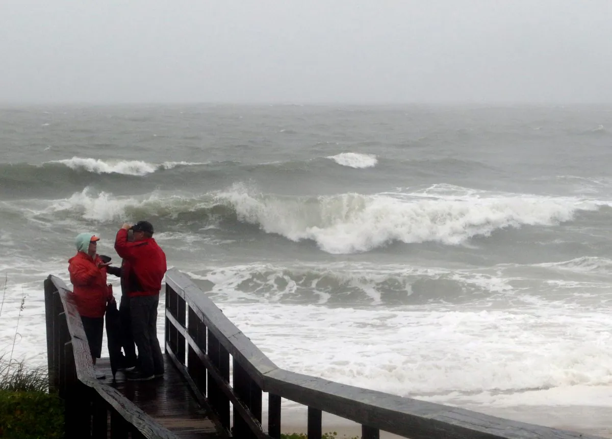 People watch the waves in a rainstorm at Atlantic Ocean at Carolina Beach, N. C., Friday, Oct. 2, 2015. (AP Photo/Harry Hamburg)