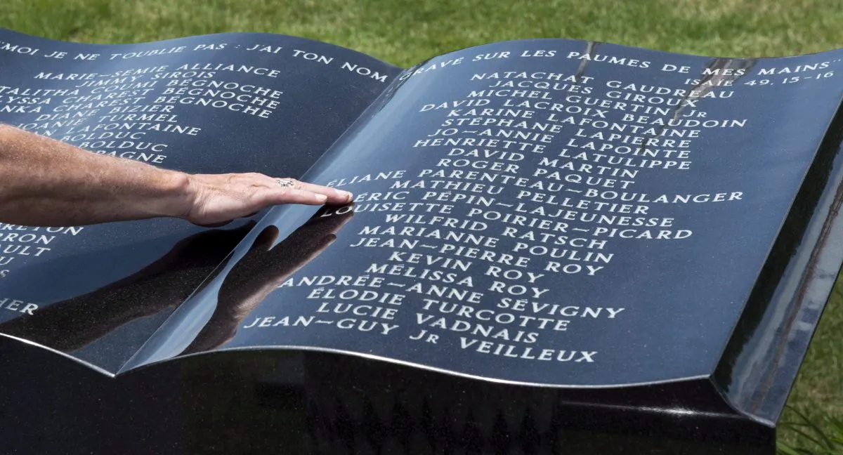 A man touches a stone monument in front of Ste-Agnes church in Lac-Megantic following a memorial service for the 47 victims of the train derailment a year ago, July 6, 2014. A Quebec judge has given his final approval regarding the terms of the $450-million settlement fund for victims and creditors of the Lac-Megantic rail disaster. (The Canadian Press/Paul Chiasson)
