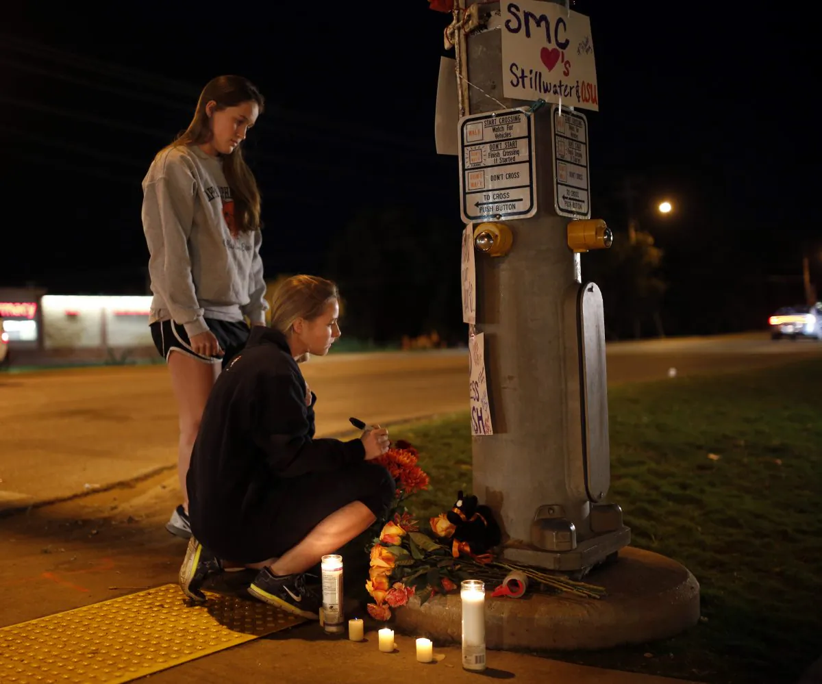 Oklahoma State students Kelly Cooke, right, and Rebecca Buchanan read messages on a memorial in Stillwater, Okla., Saturday, Oct. 24, 2015, near where a car crashed into spectators during the Oklahoma State University homecoming parade killing multiple and injuring several others. (Sarah Phipps/The Oklahoman via AP)