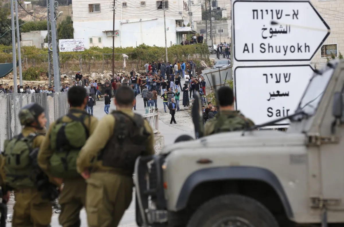 Israeli soldiers and Palestinians stand at the scene of a stabbing attack, in the West Bank settlement of Kiryat Arba, Monday, Oct. 26, 2015. The Israeli military said a Palestinian stabbed an Israeli in the West Bank before being shot and killed. According to the military, the Israeli was stabbed in the neck Monday and "severely wounded" near the city of Hebron. (AP Photo/Wisam Hashlamoun)