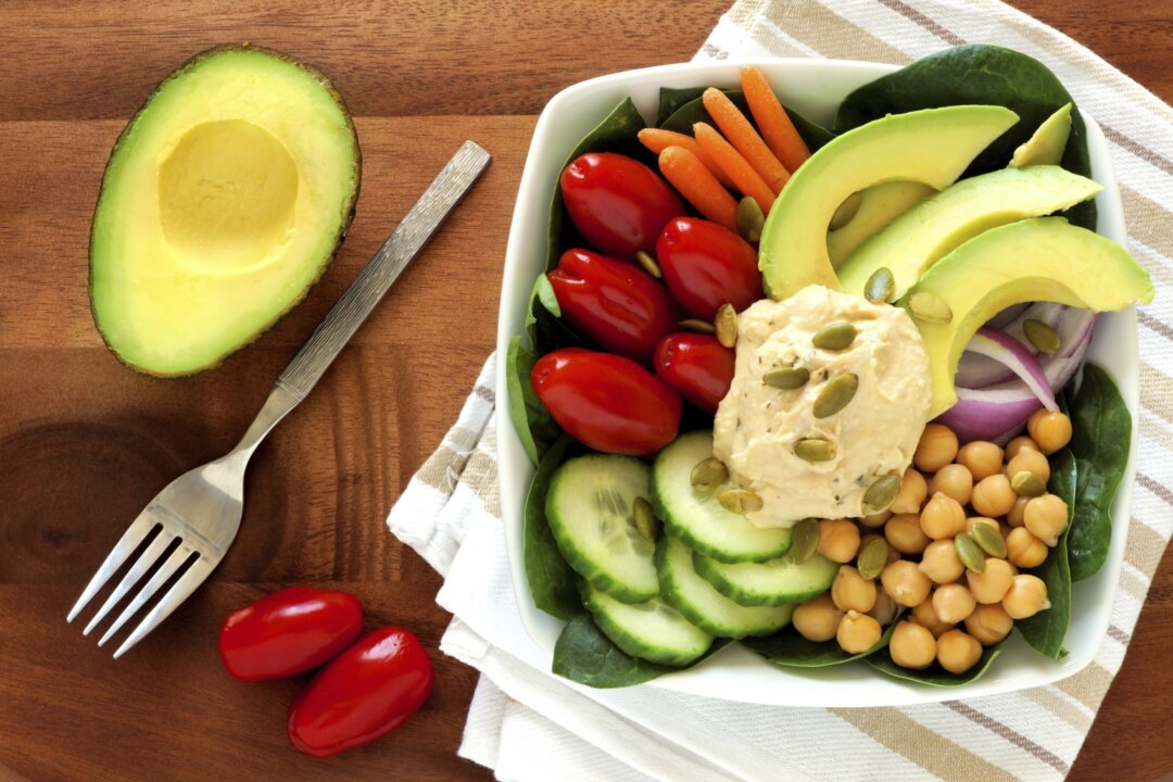 Healthy lunch bowl with avocado, hummus and fresh vegetables, overhead scene on wooden table