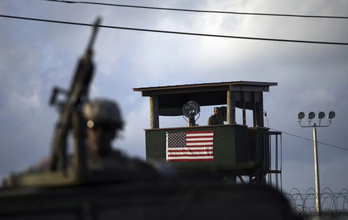 A U.S. trooper mans a machine gun in the turret on a vehicle as a guard looks out from a tower in front of the detention facility at Guantanamo Bay U.S. Naval Base, Cuba, on March 30, 2010. (AP Photo/Brennan Linsley)