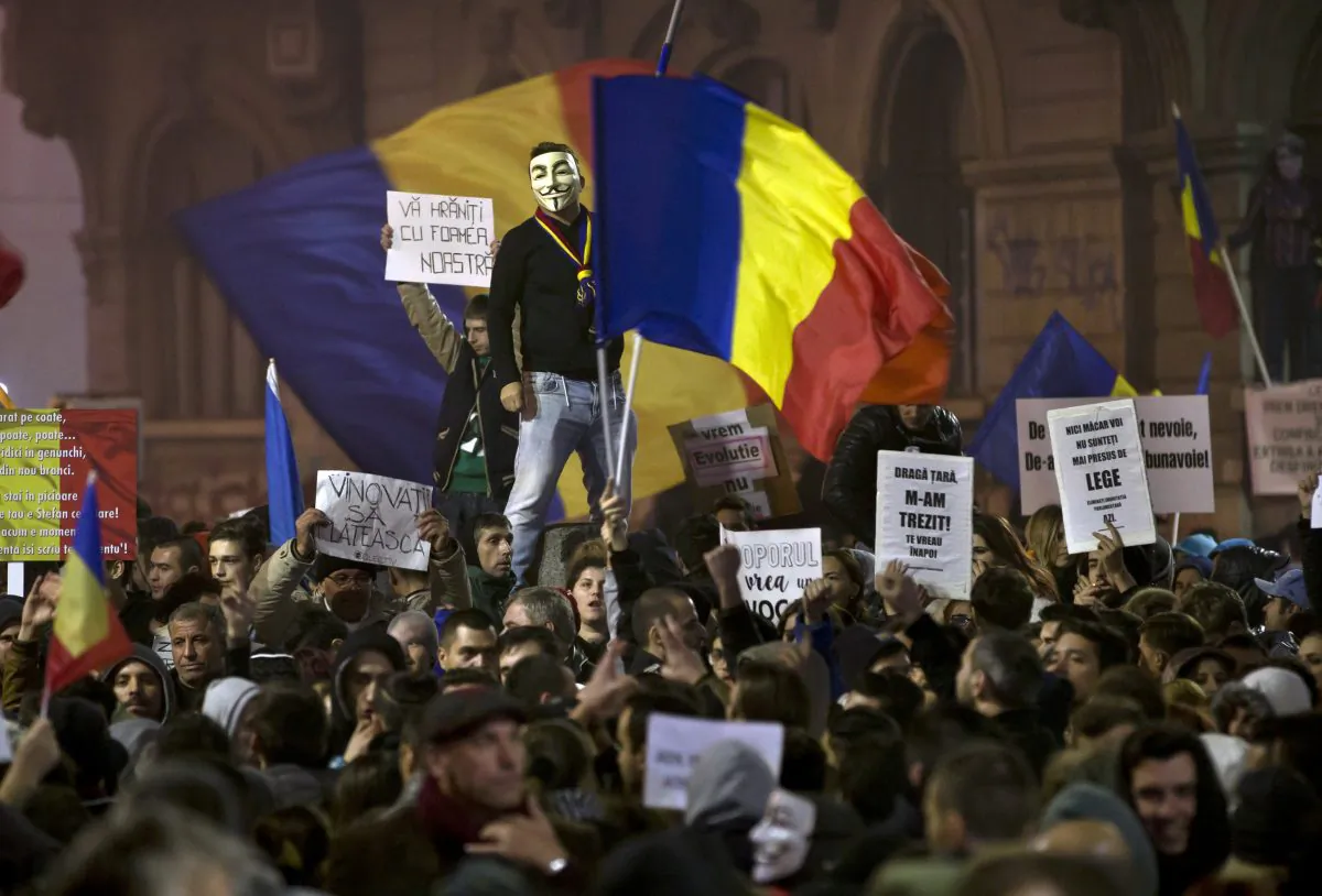 A man wearing a Guy Fawkes mask stands above protesters shouting slogans against the Romanian politicians during the fourth day of protests, joined by tens of thousands across the country, calling for early elections, in Bucharest, Romania, on Nov. 6, 2015. Large street protests followed the Oct. 30 nightclub fire, which many Romanians blame on a weak enforcement of regulations and corruption. The street protesters have condemned the nation’s politicians as arrogant and corrupt and isolated from the problems of ordinary people. Banners read "You are feeding on our hunger," top left, and "The culprits must pay," bottom left. (AP Photo/Vadim Ghirda)