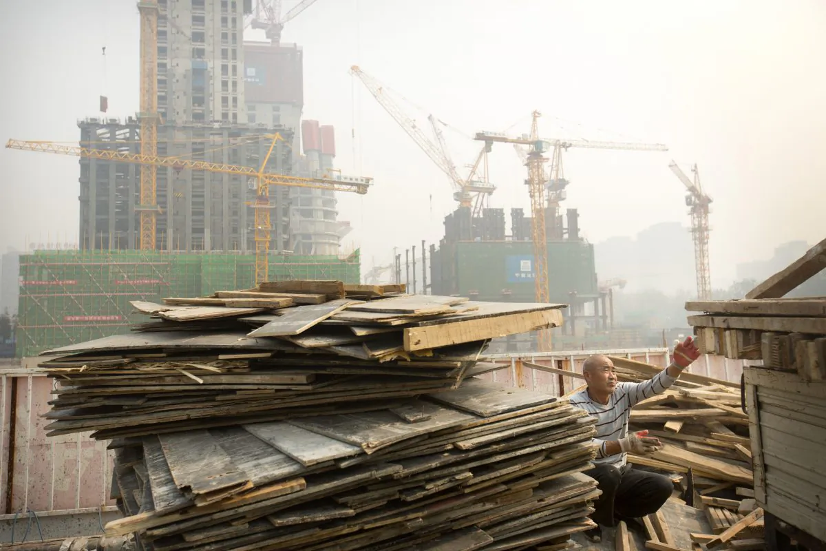 A worker tosses boards onto the back of a truck at a construction site in Beijing on Oct. 6, 2015. (AP Photo/Mark Schiefelbein)