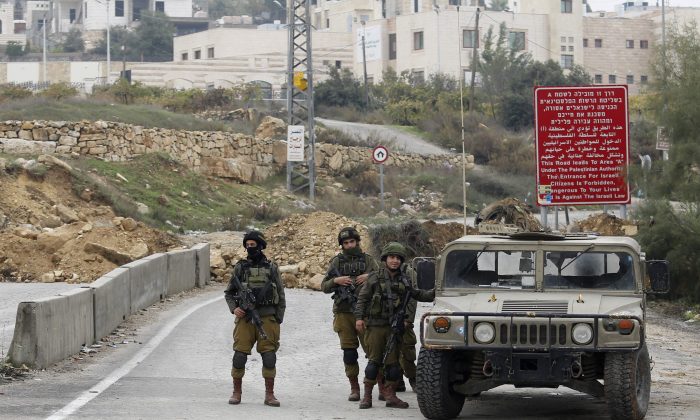 Israeli soldiers stand guard after the military blocked the road with an earth berm at one of the exits of the West Bank city of Hebron, on Nov. 7, 2015. Three incidents took place Friday in Hebron, the West Bank's largest city, which has been the main area of friction in recent weeks. Hundreds of combat troops guard about 850 Jewish settlers in the center of Hebron where they live amid tens of thousands of Palestinians. (AP Photo/Nasser Shiyoukhi)