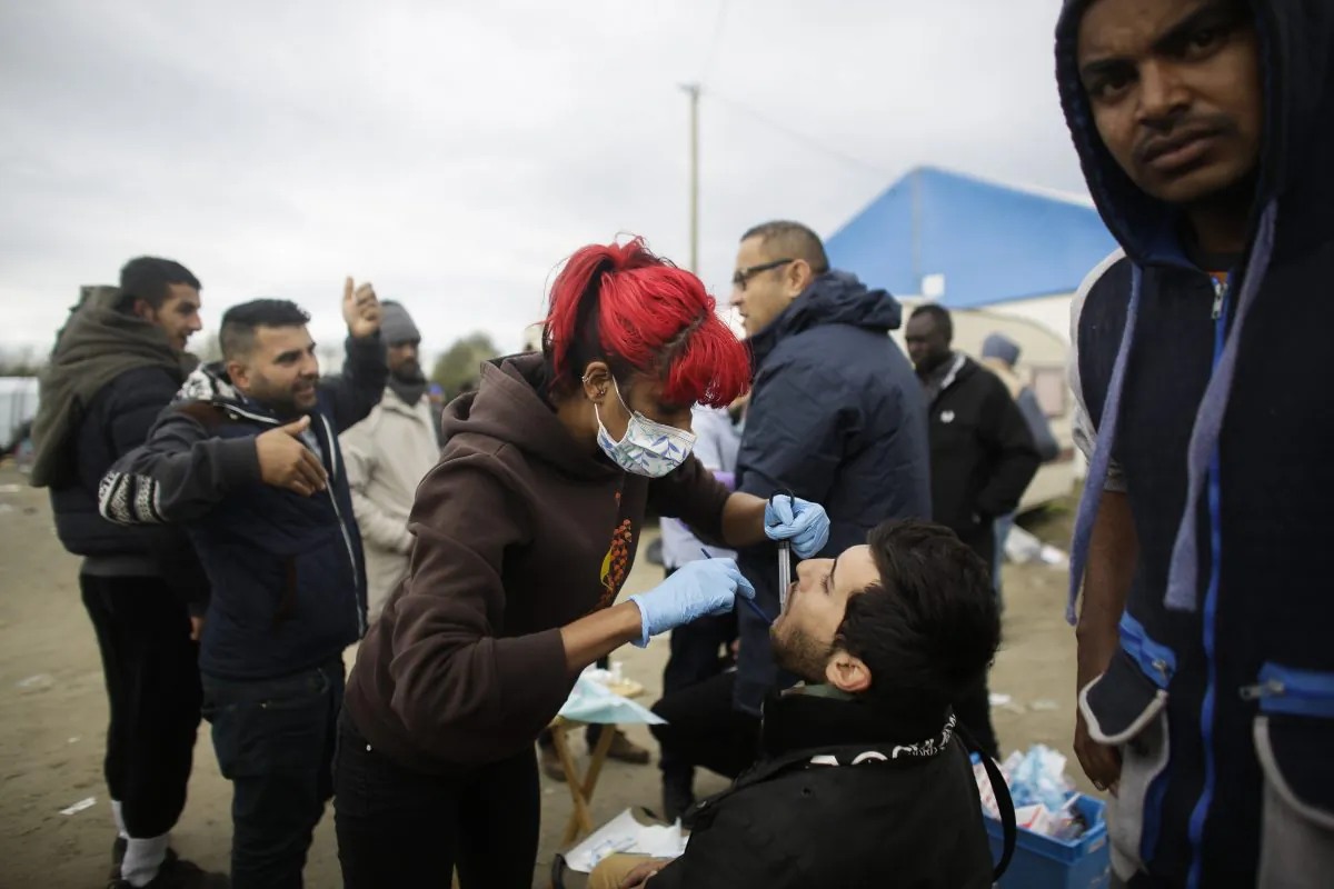 In this Saturday, Nov. 7, 2015 photo dentist Raid Ali, center right, and his colleague Aliyo Rashid Taylor, center left, treat migrants with toothache inside France's biggest refugee camp near Calais, northern France. (AP Photo/Markus Schreiber)