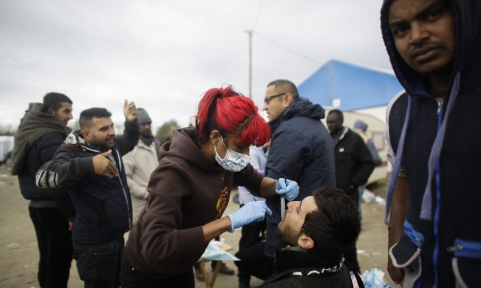In this Saturday, Nov. 7, 2015 photo dentist Raid Ali, center right, and his colleague Aliyo Rashid Taylor, center left, treat migrants with toothache inside France's biggest refugee camp near Calais, northern France. (AP Photo/Markus Schreiber)
