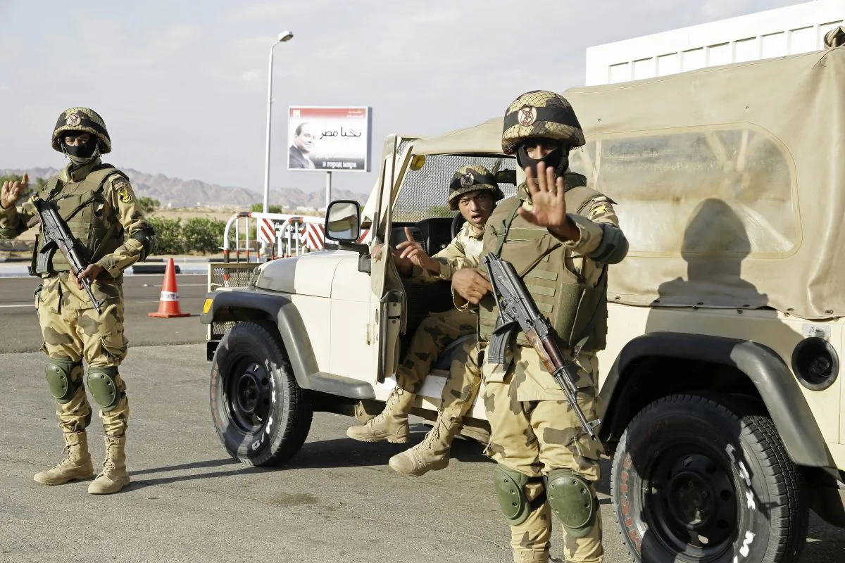 Egyptian soldiers guarding the entrance to the Sharm el-Sheikh International Airport gesture to a photographer in south Sinai, Egypt, on Nov. 6, 2015. The sign has a picture of Egyptian President Abdel Fattah el-Sissi and a slogan in Arabic which reads, "Long Live Egypt." Startling public criticism in Egypt points to how the aura of invincibility that President el-Sissi has long enjoy appears to be eroding. The criticisms spring from multiple fronts—complaints over neglect by officials, an economy that hasn’t seen dramatic improvement and now worries over tourism following the crash of a Russian jet in Sinai. (AP Photo/Thomas Hartwell)