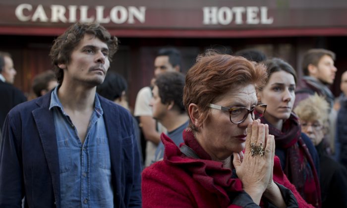 People pay their respect to the victims of the the attacks on restaurant Le Petit Cambodge (Little Cambodia) and the Carillon Hotel, rear, on the first of three days of national mourning in Paris, Sunday, Nov. 15, 2015. (AP Photo/Peter Dejong)