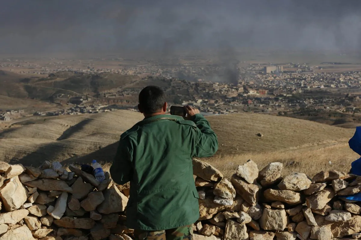 A Kurdish fighter records smoke rising over Sinjar, northern Iraq from oil fires set by Islamic State militants as Kurdish Iraqi fighters, backed by U.S.-led airstrikes, launch a major assault on Thursday, Nov. 12, 2015. The strategic town of Sinjar was overran last year by the Islamic State group in an onslaught that caused the flight of tens of thousands of Yazidis and first prompted the United States to launch the air campaign against the militants. (AP Photo/Bram Janssen)