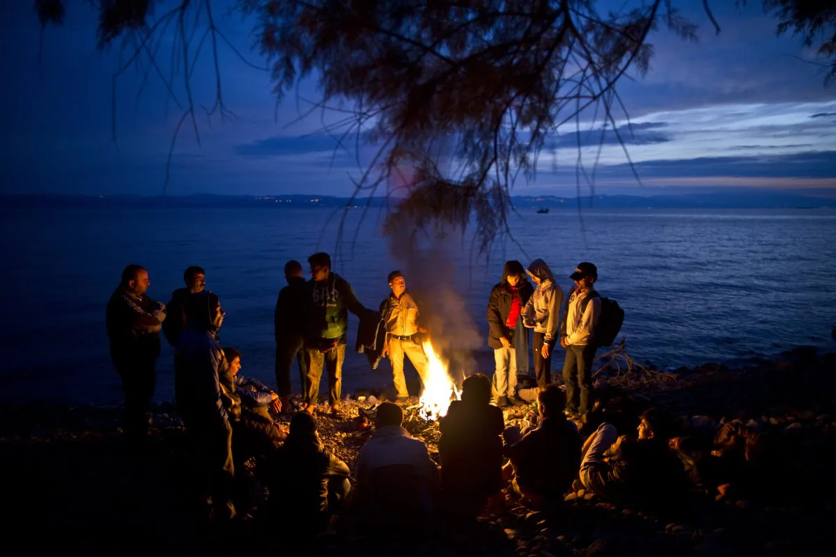 Syrian and Afghan refugees warm themselves and dry their clothes around a fire after arriving on a dinghy from the Turkish coast to the northeastern Greek island of Lesbos, on Oct. 7, 2015. (AP Photo/Muhammed Muheisen)