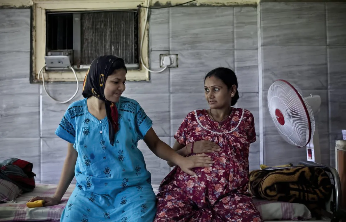 In this Nov. 2, 2015 photo, 30-year-old Bhagwati Chauhan, who gave birth to a Canadian couple's child on Oct. 27, touches the 9-month pregnant belly of 35-year-old Chandrika Makwana, who is carrying twins for an American couple, at the Akanksha Clinic, one of the most organized clinics in the surrogacy business, in Anand, India. Chauhan, whose husband died recently, plans to use the money she will earn as a surrogate to buy a house and send her son to school. The Indian government recently banned surrogate services for foreigners and ordered fertility clinics to stop the practice of hiring Indian women to bear children for them. (AP Photo/Allison Joyce)