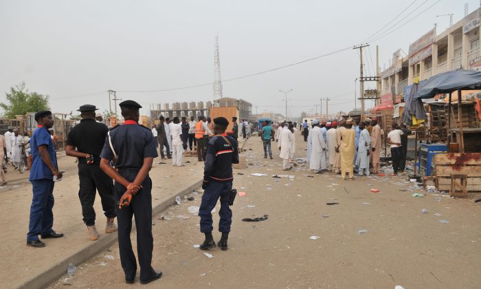 Security officers stand guard at the scene of an explosion at a mobile phone market in Kano, Nigeria, on Wednesday, Nov. 18, 2015. The suicide bomber exploded as truckers were tucking into dinner at the bustling marketplace where vendors urged them to buy sugar cane. At least 34 people were killed and another 80 wounded in Yola, a town packed with refugees from Nigeria's Islamic uprising, emergency officials said Wednesday. Later Wednesday, two more suicide bombers killed at least 15 people in the northern city of Kano and injured 53, according to police. (AP Photo/Muhammed Giginyu)