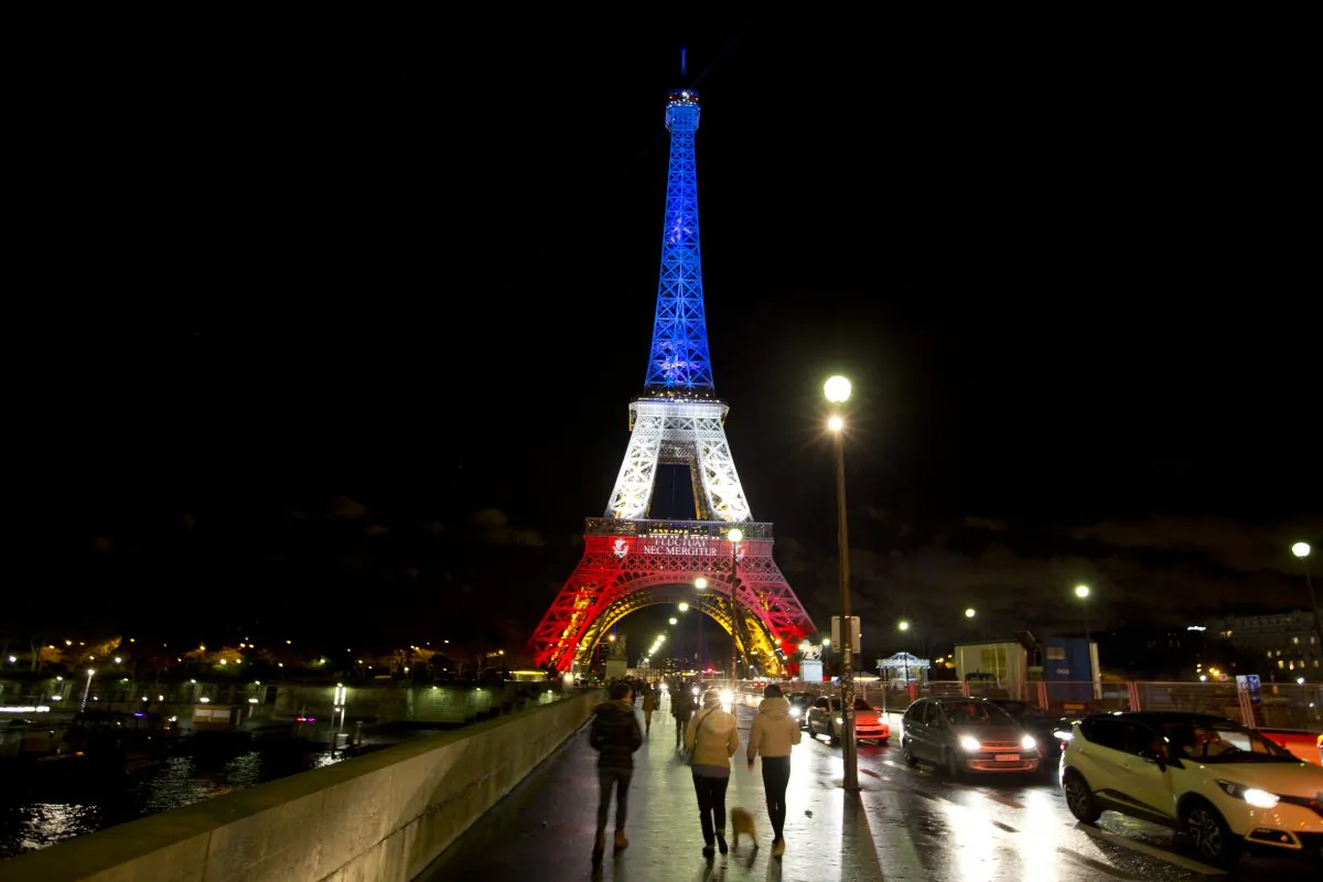 People walk towards the illuminated Eiffel Tower in the French national colors red, white, and blue on Nov. 17, 2015, in honor of the victims of Paris attacks of Nov. 13. (AP Photo/Peter Dejong)