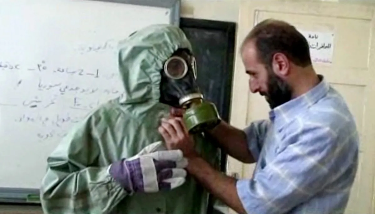 FILE - This image made from an AP video posted on Wednesday, Sept. 18, 2013 shows a volunteer adjusting a students gas mask and protective suit during a session on reacting to a chemical weapons attack, in Aleppo, Syria.