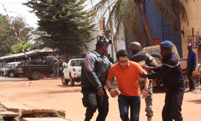 Mali trooper assist a hostage, centre, to leave the scene, from the Radisson Blu hotel to safety after gunmen attacked the hotel in Bamako, Mali, Friday, Nov. 20, 2015. Islamic extremists armed with guns and throwing grenades stormed the Radisson Blu hotel in Mali's capital Friday morning, killing at least three people and initially taking numerous hostages, authorities said.  (AP Photo/Harouna Traore)