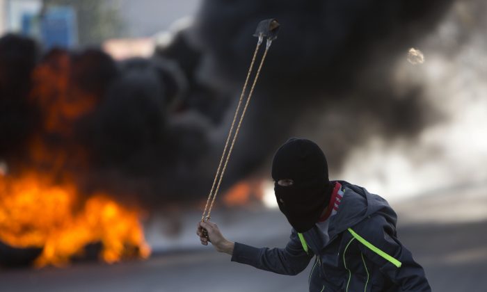 A Palestinian protester uses a sling shot to hurl stones at Israeli troops during clashes, in the West Bank city of Ramallah, Friday, Nov. 20, 2015. (AP Photo/Majdi Mohammed)