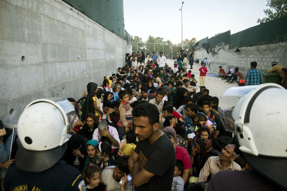 Migrants are guarded by Greek policemen as they wait to be registered at a camp set up for migrants from Afghanistan near Moria on the island of Lesbos, Greece, on Oct. 7, 2015. (Zoltan Balogh/MTI via AP)