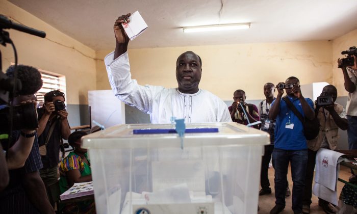 Burkina Faso presidential candidate from the UPC party Zephirin Diabre (C) holds up his ballot before he casts it during elections in Ouagadougou,  Burkina Faso, Sunday, Nov. 29, 2015. (AP Photo/Theo Renaut)
