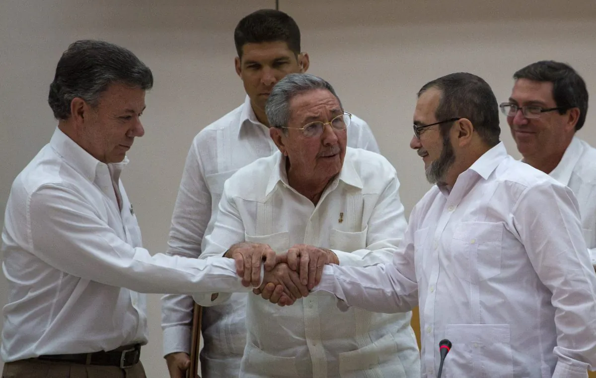 Cuba's President Raul Castro, center, encourages Colombian President Juan Manuel Santos (L) and Commander the Revolutionary Armed Forces of Colombia or FARC, Timoleon Jimenez, known as  "Timochenko", to shake hands, in Havana, Cuba, on Sept. 23, 2015. (AP Photo/Desmond Boylan, File)