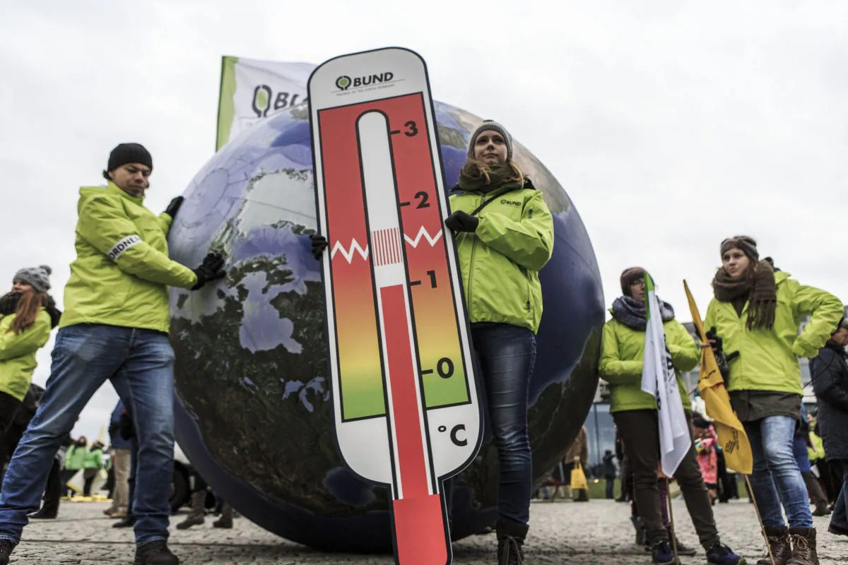 A woman stands in front of a model of the Earth holding a thermometer as activists participate in the Global Climate March in Berlin, Germany, on Nov. 29, 2015. (Carsten Koall/Getty Images)