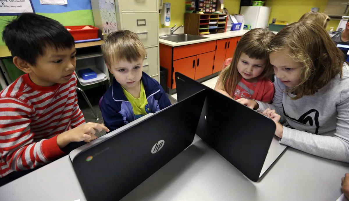 In this photo taken Nov. 4, 2015, second grader Josh Mercado, left, helps kindergartner Erik Hodges, as second grader Annabelle Davis, right, helps kindergartner Kaidyance Harris, on programming during their weekly computer science lesson at Marshall Elementary School in Marysville, Wash. (AP Photo/Elaine Thompson)