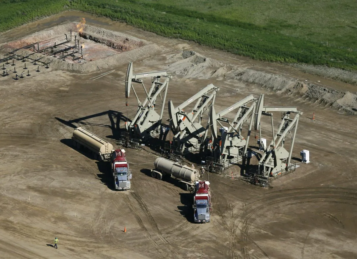 A pair of tanker trucks parked next to pumps at an oil-producing well in McKenzie County, N.D., on June 12, 2014. Lower fossil fuel prices have come at a painful cost: 122,300 lost jobs in the energy sector over the past year. Average wages have tumbled 1.5 percent to $26.72 an hour for energy production workers who kept their jobs, even as workers nationwide are earning slightly more money than a year ago. The November 2015 jobs report showed the sharp contrast between the overall economy and the ailing fossil fuels industry.(AP Photo/Charles Rex Arbogast)