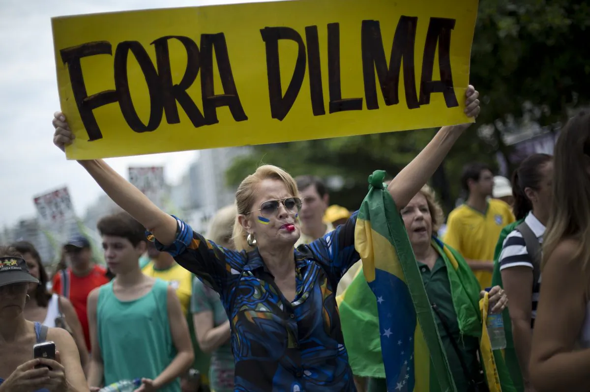A woman holds a sign that reads "Dilma Out" during a demonstration for the impeachment of Brazil’s President Dilma Rousseff on Copacabana beach in Rio de Janeiro, Brazil, Sunday, Dec. 13, 2015. Dozens of cities are staging protests across Brazil asking Congress to impeach President Dilma Rousseff. Thousands have gathered Sunday in cities such as Brasilia, Rio de Janeiro, and Sao Paulo wearing the Brazilian flag colors. They are holding banners that criticize the president and her Workers' Party for a series of massive corruption scandal. (AP Photo/Silvia Izquierdo)